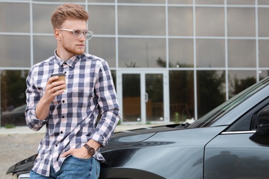 Photo of Attractive young man with cup of coffee near luxury car outdoors