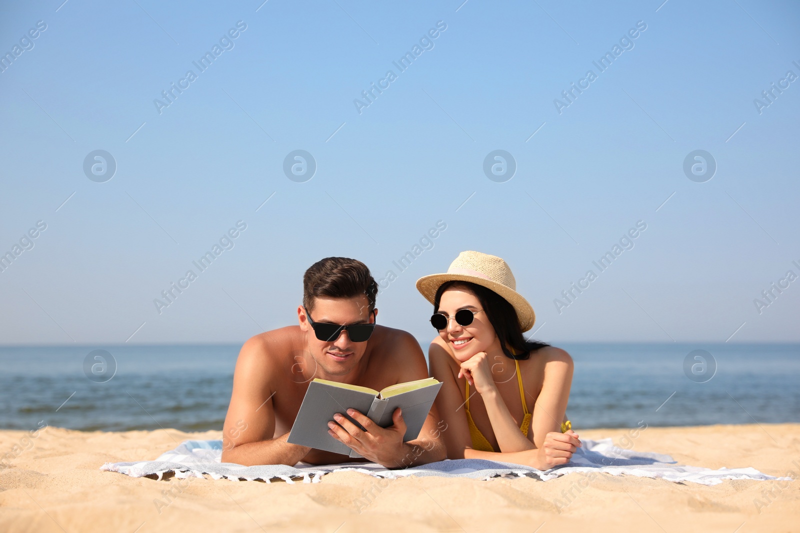 Photo of Happy couple reading book together on sunny beach