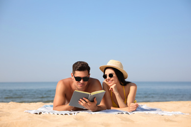Photo of Happy couple reading book together on sunny beach