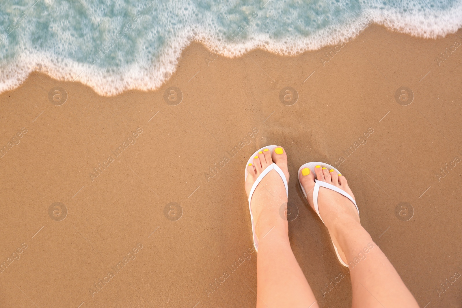 Photo of Top view of woman with white flip flops on sand near sea, space for text. Beach accessories