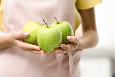 Photo of Woman holding ripe green apples indoors, closeup