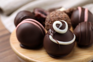 Many different delicious chocolate truffles on wooden plate, closeup