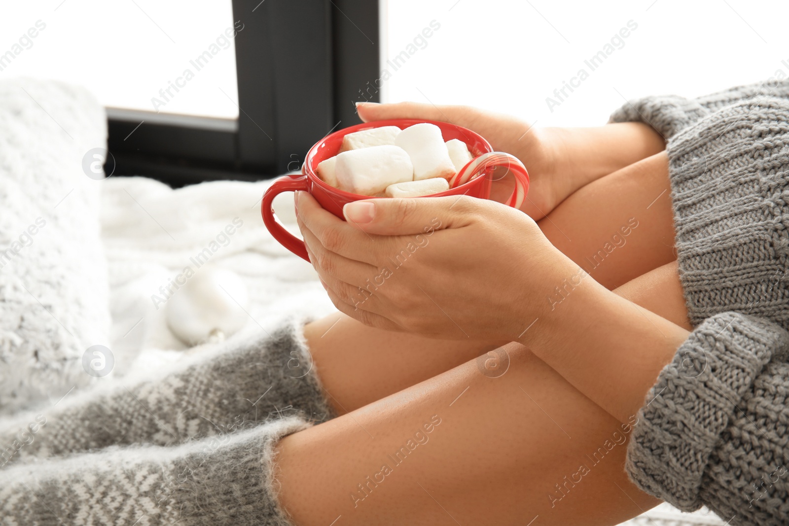 Photo of Woman relaxing with cup of hot winter drink on knitted plaid. Cozy season