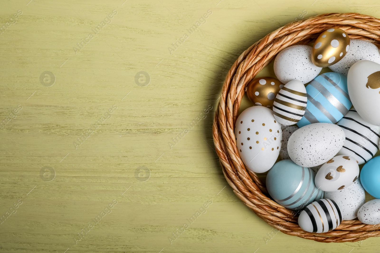 Photo of Decorative nest and many beautiful Easter eggs on yellow wooden table, top view. Space for text