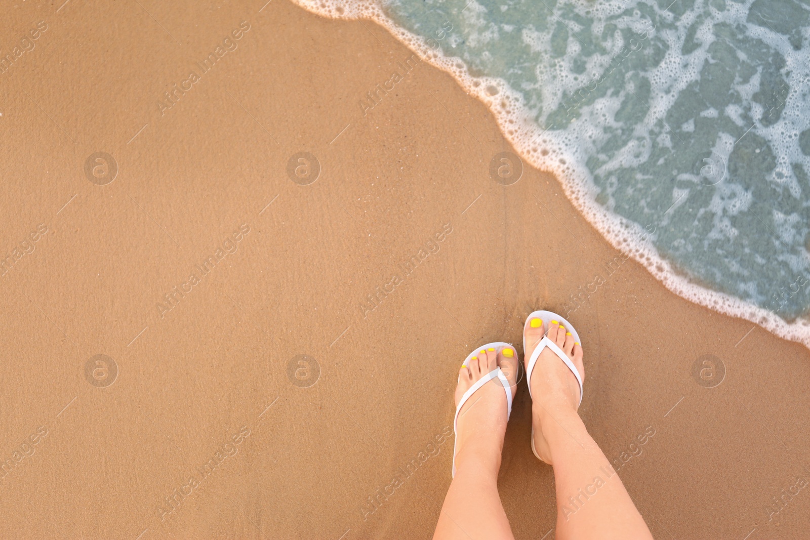 Photo of Top view of woman with white flip flops on sand near sea, space for text. Beach accessories