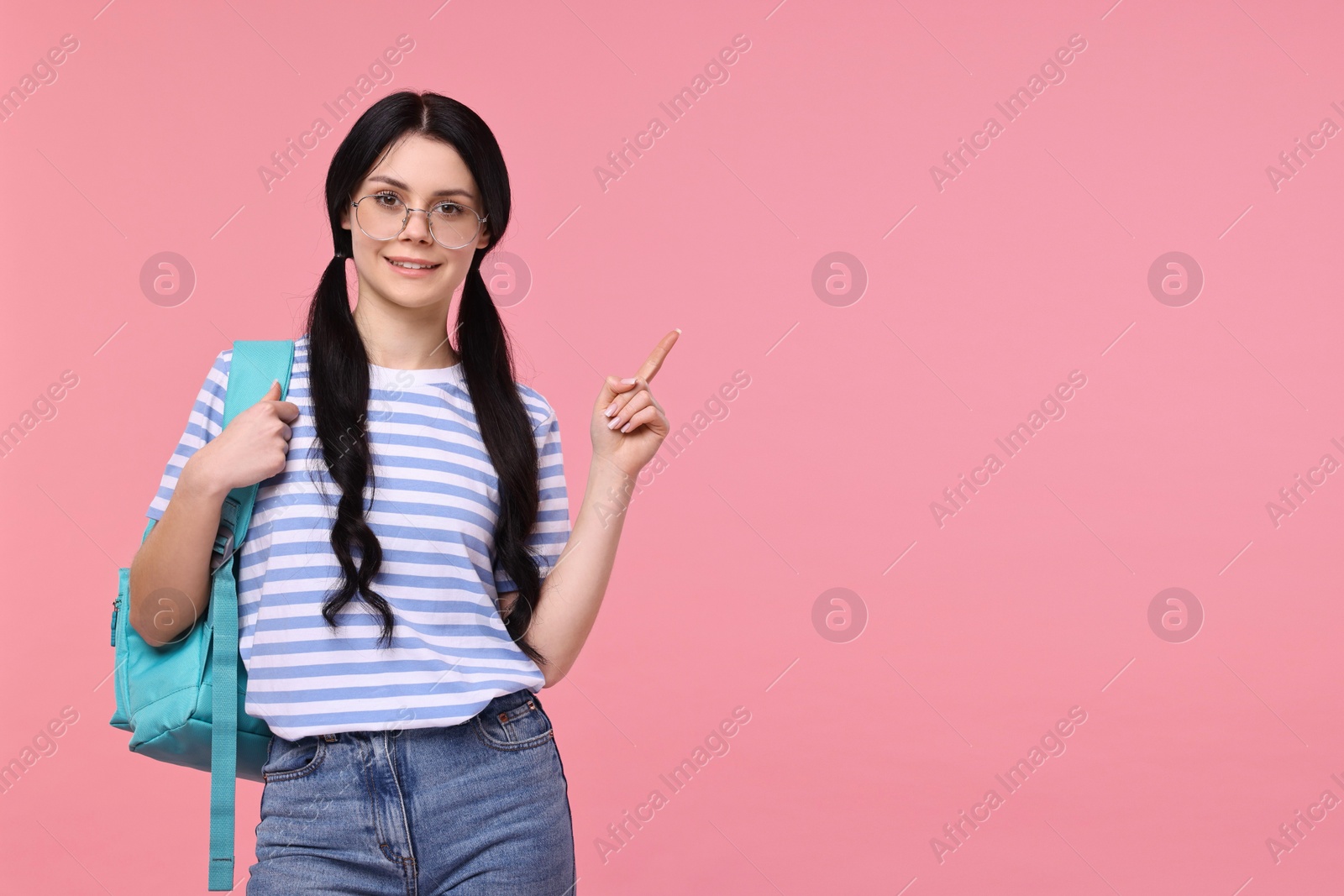 Photo of Smiling student with backpack pointing at something on pink background. Space for text