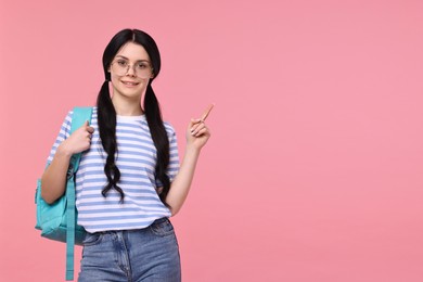 Smiling student with backpack pointing at something on pink background. Space for text