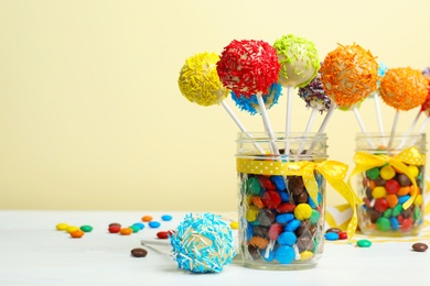 Photo of Glass jars with tasty cake pops and dragee on table against yellow background, space for text