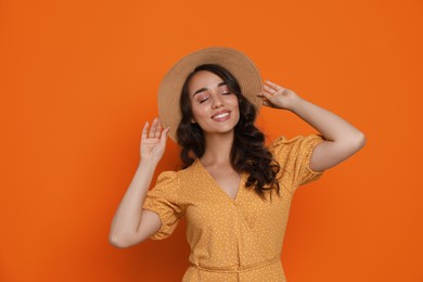 Image of Beautiful young woman with straw hat on orange background