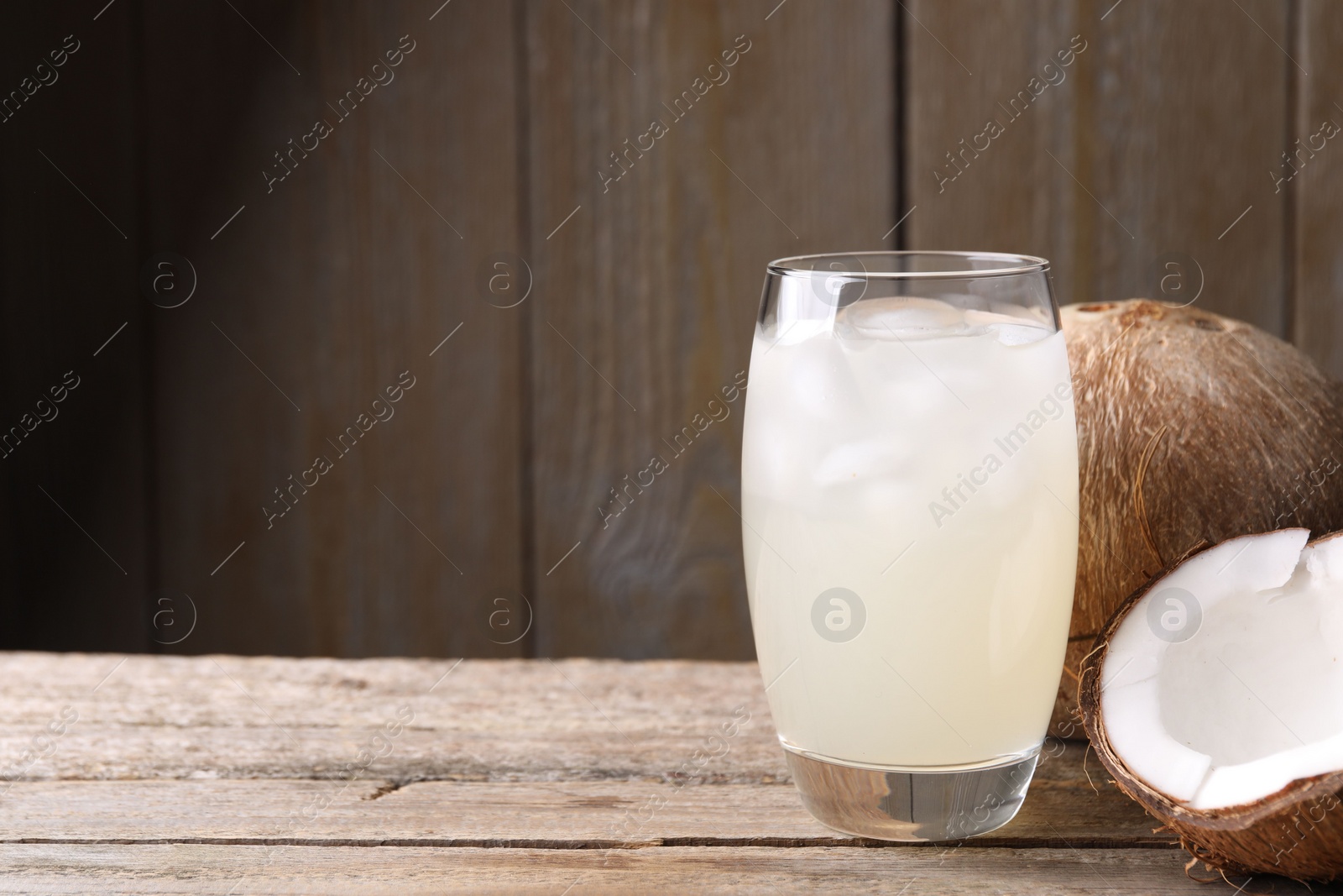 Photo of Glass of coconut water, ice cubes and nuts on wooden table, space for text