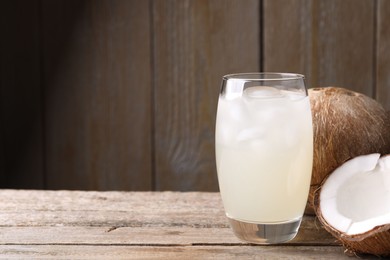 Glass of coconut water, ice cubes and nuts on wooden table, space for text