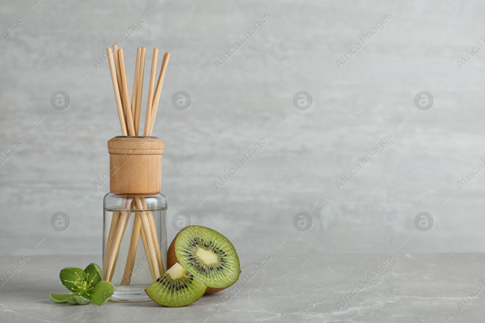Photo of Aromatic reed freshener and kiwi on table against grey background. Space for text