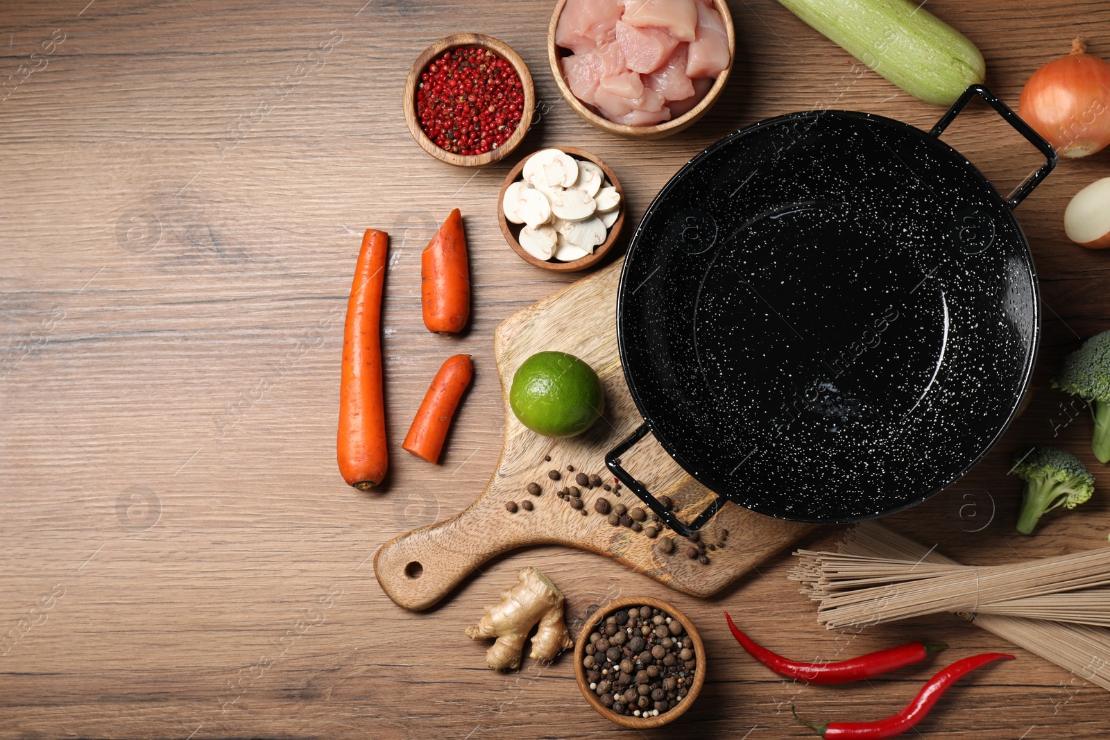 Photo of Empty iron wok surrounded by raw ingredients on wooden table, flat lay. Space for text