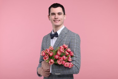 Happy young man with beautiful bouquet on pink background