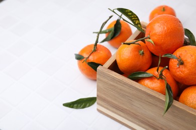 Photo of Wooden crate with fresh ripe tangerines and leaves on white table, closeup. Space for text