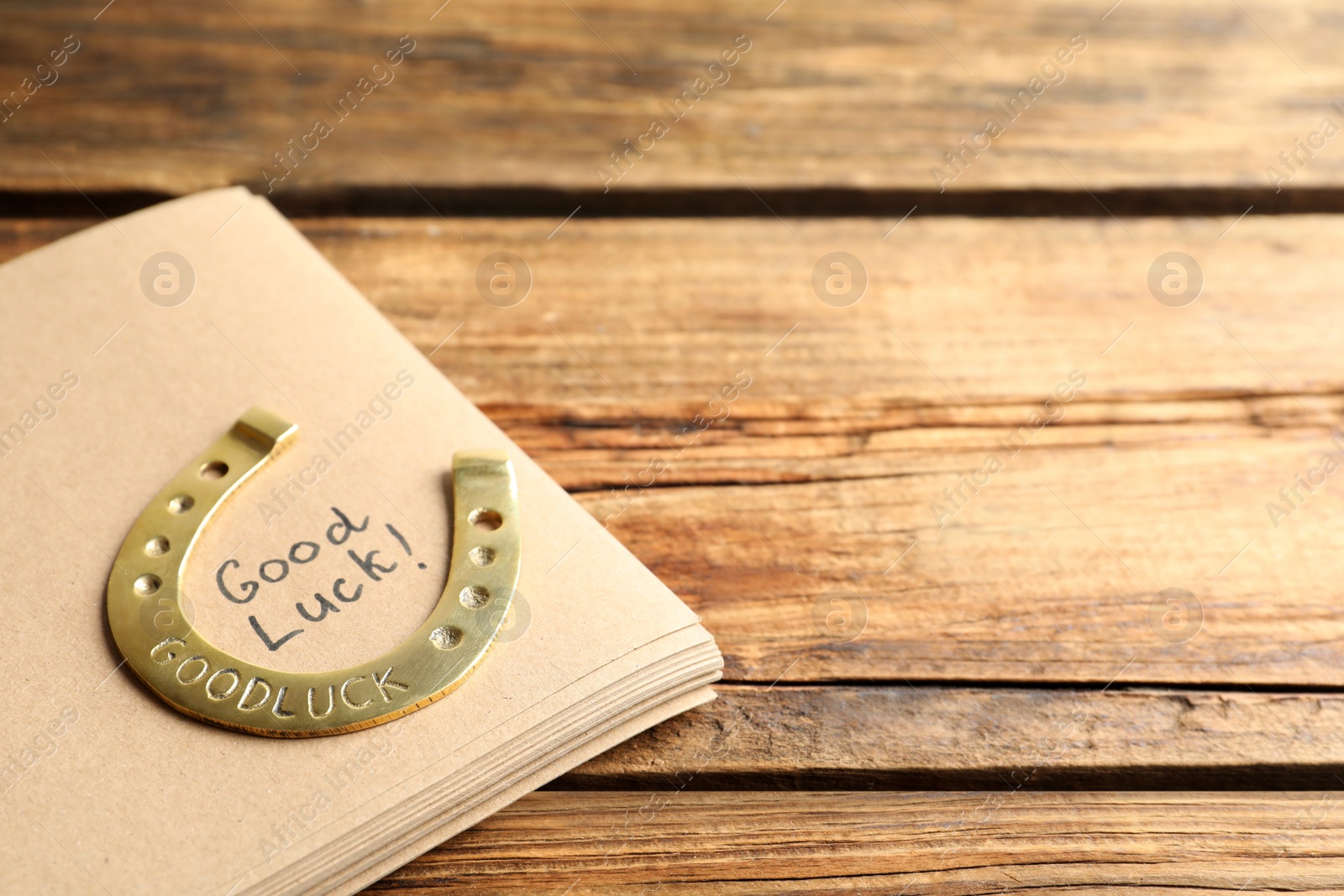 Photo of Notebook with phrase GOOD LUCK and horseshoe on wooden table, closeup. Space for text