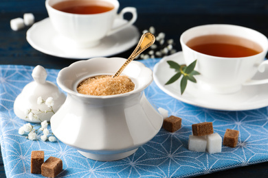 Ceramic bowl with brown sugar and cups of tea on table