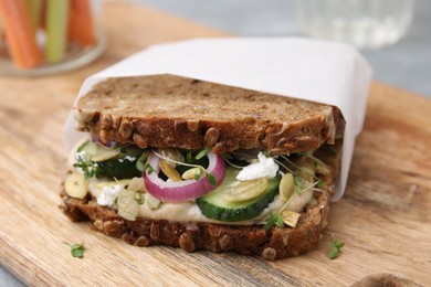 Photo of Tasty vegan sandwich with cucumber, onion, hummus and pumpkin seeds on wooden board, closeup