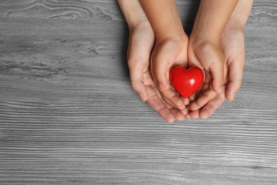 Woman and child holding heart on wooden background, top view with space for text. Donation concept