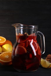 Glass jug of aromatic punch drink and ingredients on black table