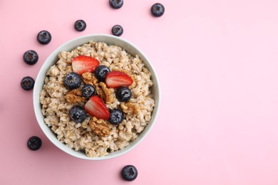 Photo of Tasty oatmeal with strawberries, blueberries and walnuts in bowl surrounded by fresh berries on pink background, flat lay. Space for text