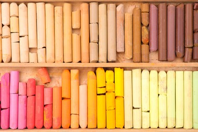 Photo of Set of soft pastels in wooden box as background, top view. Drawing material