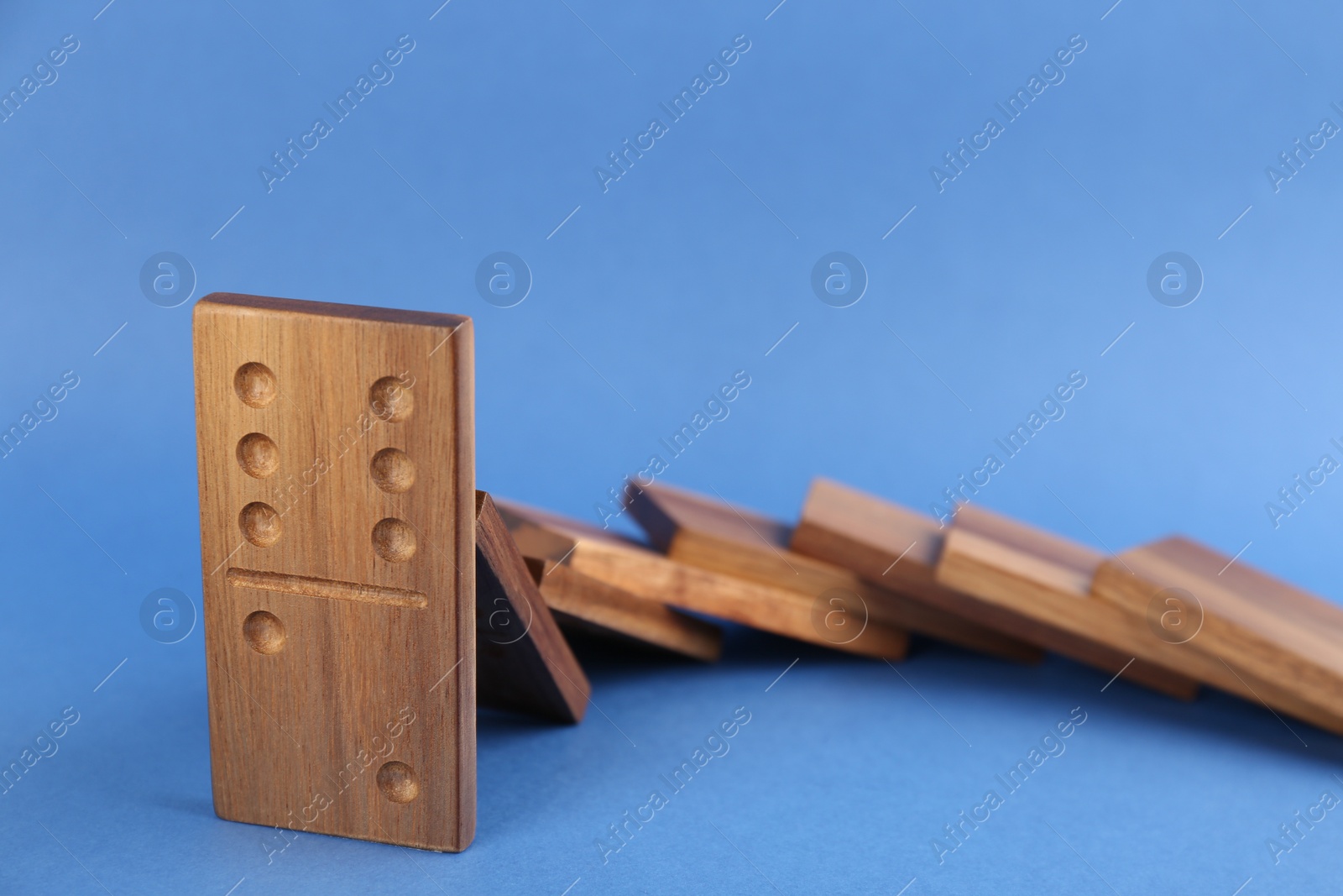 Photo of Wooden domino tiles falling on blue background, closeup. Space for text