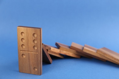 Wooden domino tiles falling on blue background, closeup. Space for text