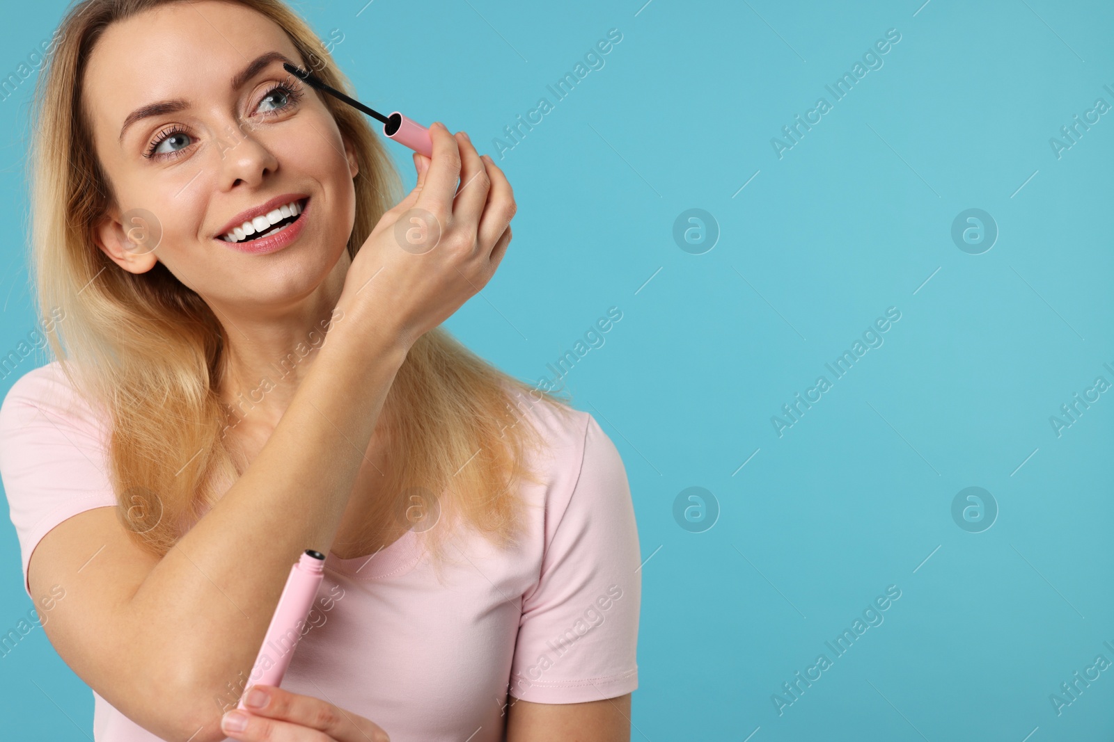 Photo of Beautiful woman applying mascara on light blue background, space for text