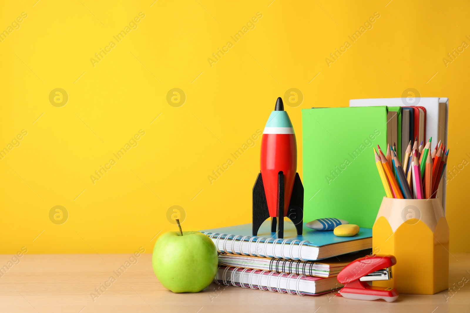 Photo of Bright toy rocket and school supplies on wooden table. Space for text