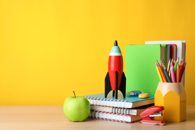 Photo of Bright toy rocket and school supplies on wooden table. Space for text