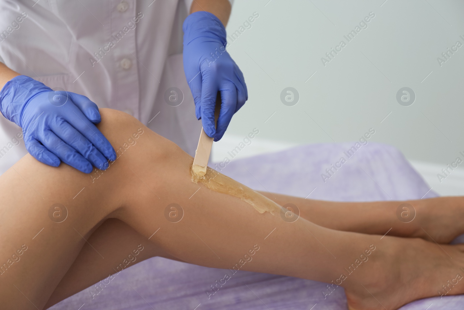 Photo of Woman getting wax epilation of legs in salon, closeup