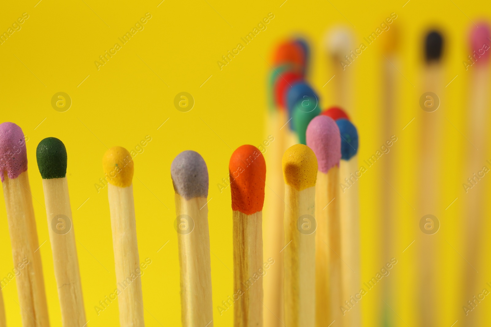 Photo of Matches with colorful heads on yellow background, closeup