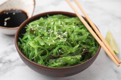 Photo of Tasty seaweed salad in bowl served on white marble table, closeup