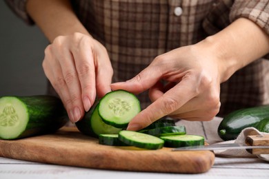 Photo of Woman putting slice of fresh cucumber onto cutting board, closeup