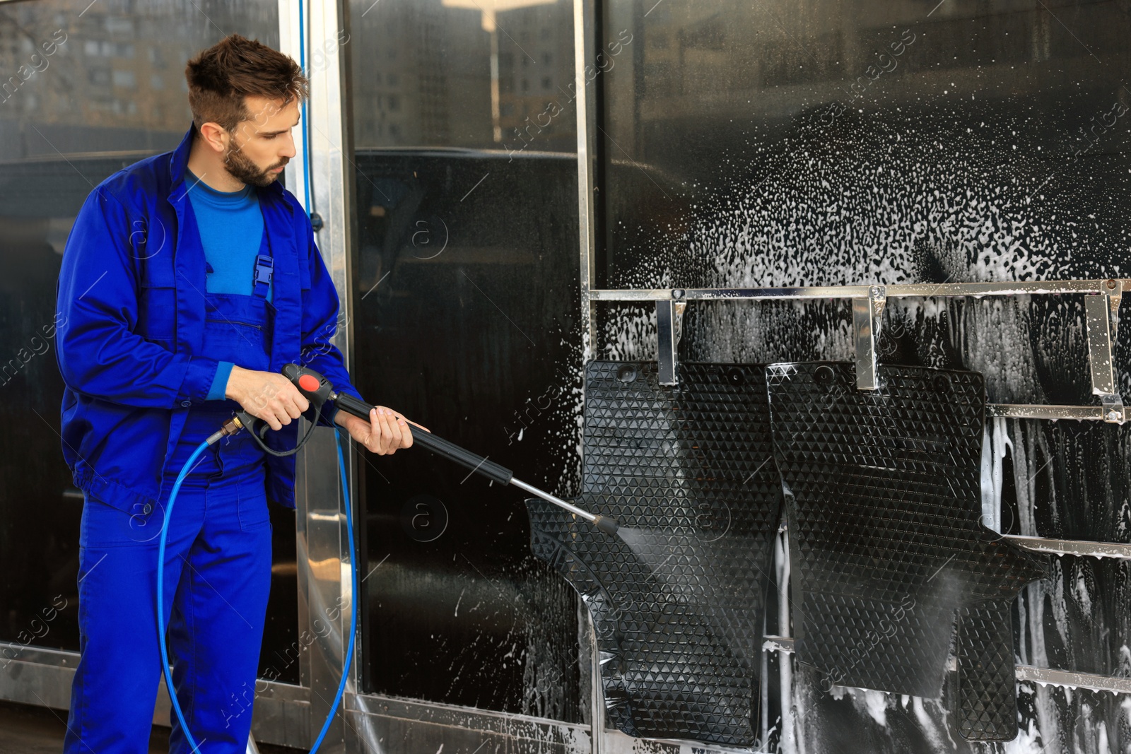 Photo of Worker cleaning auto mats with high pressure water jet at car wash
