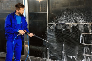 Photo of Worker cleaning auto mats with high pressure water jet at car wash