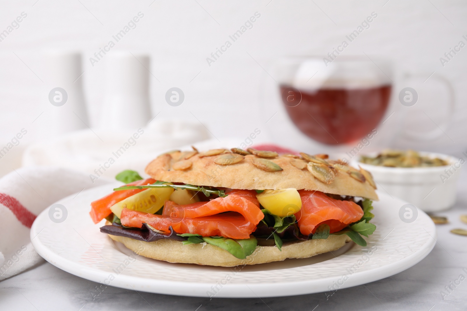 Photo of Tasty bagel with salmon and tomatoes on white marble table, closeup