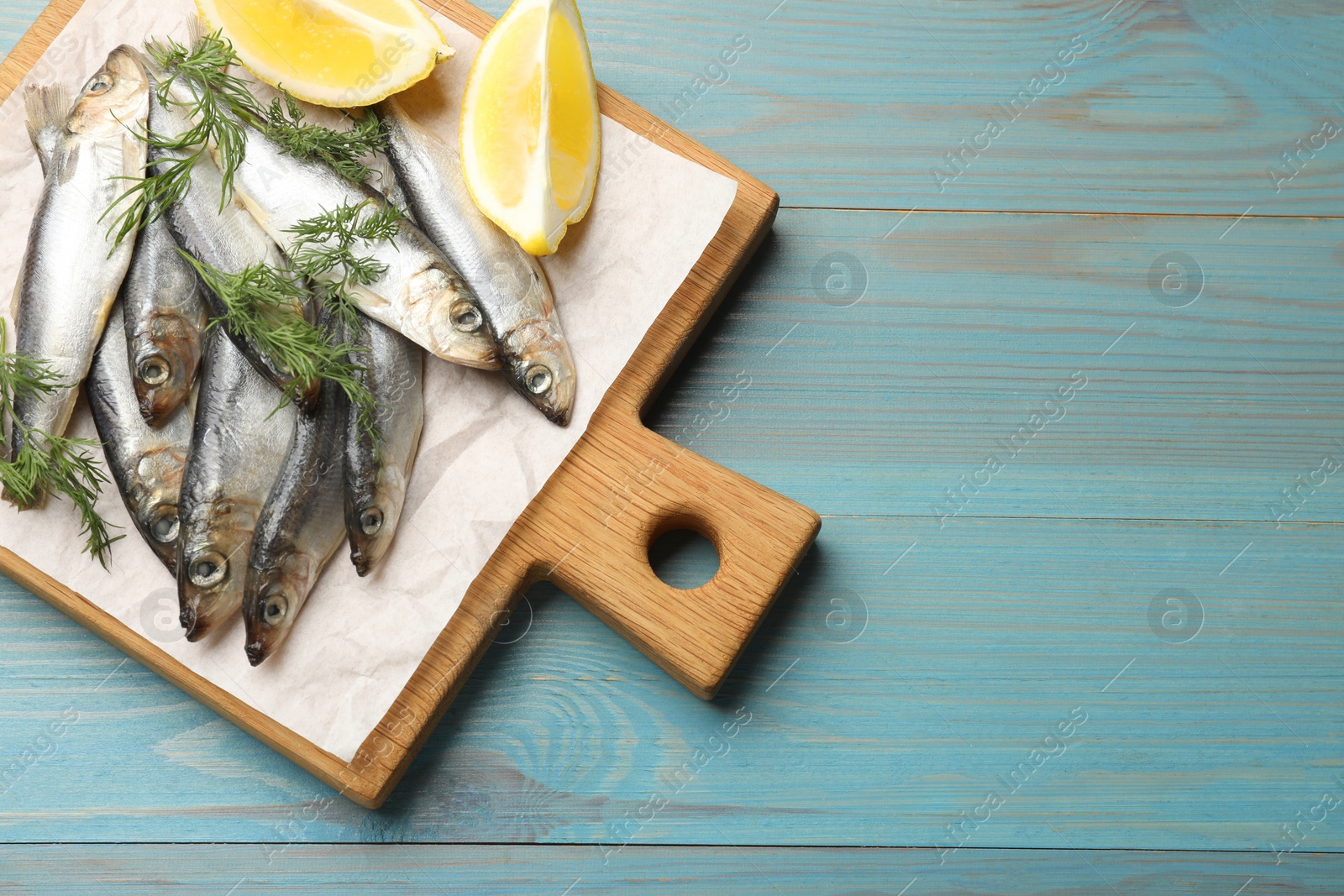 Photo of Fresh raw sprats, dill and cut lemon on light blue wooden table, top view. Space for text