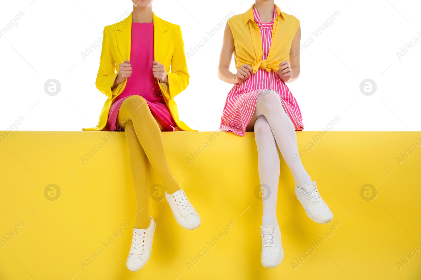 Photo of Women wearing bright tights sitting on color background, closeup