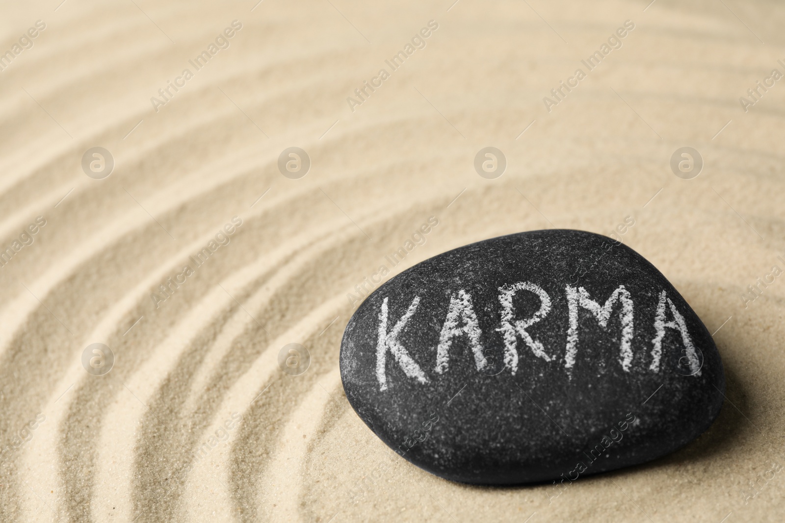 Photo of Stone with word Karma on sand, space for text