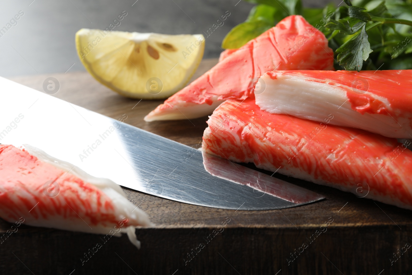 Photo of Cut crab sticks and knife on wooden board, closeup