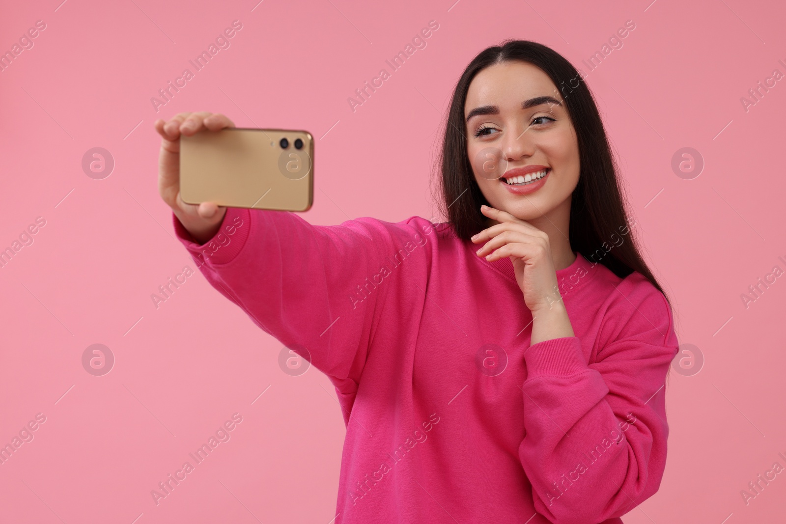 Photo of Smiling young woman taking selfie with smartphone on pink background, space for text