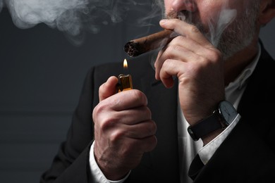 Photo of Bearded man lighting cigar on dark grey background, closeup