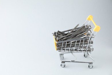 Photo of Metal nails in shopping cart on light grey background, space for text