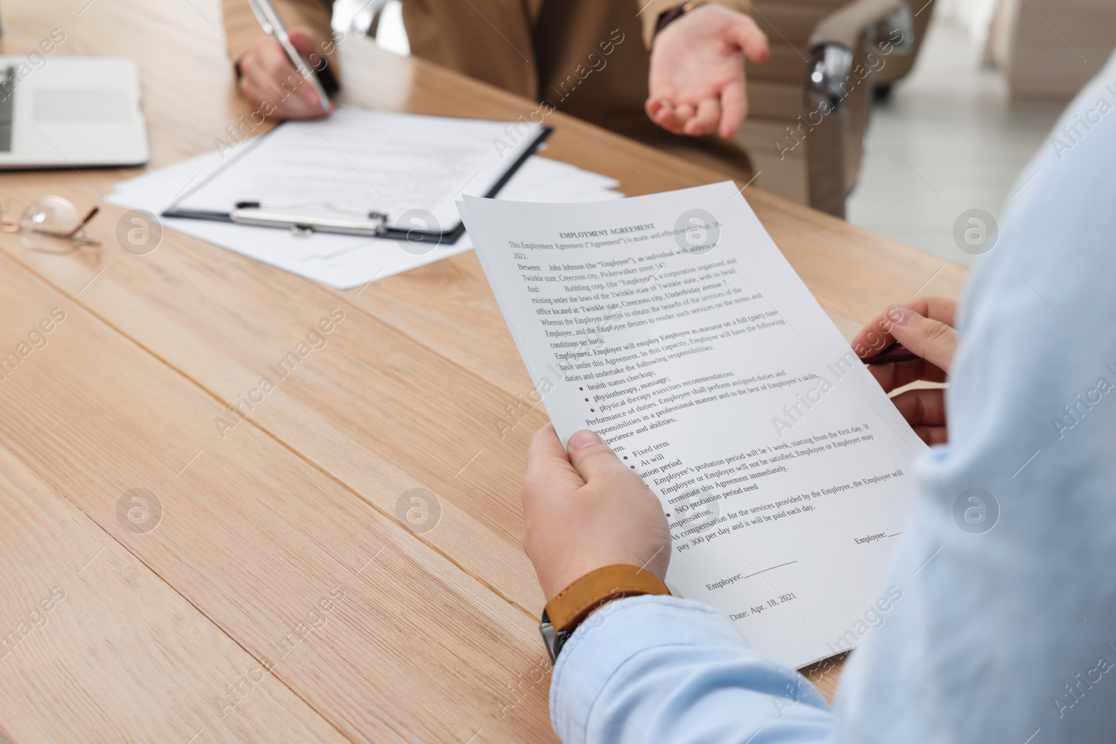 Photo of Man reading employment agreement at table in office, closeup. Signing contract