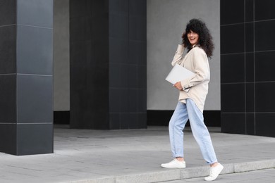 Happy young woman holding modern laptop outdoors. Space for text