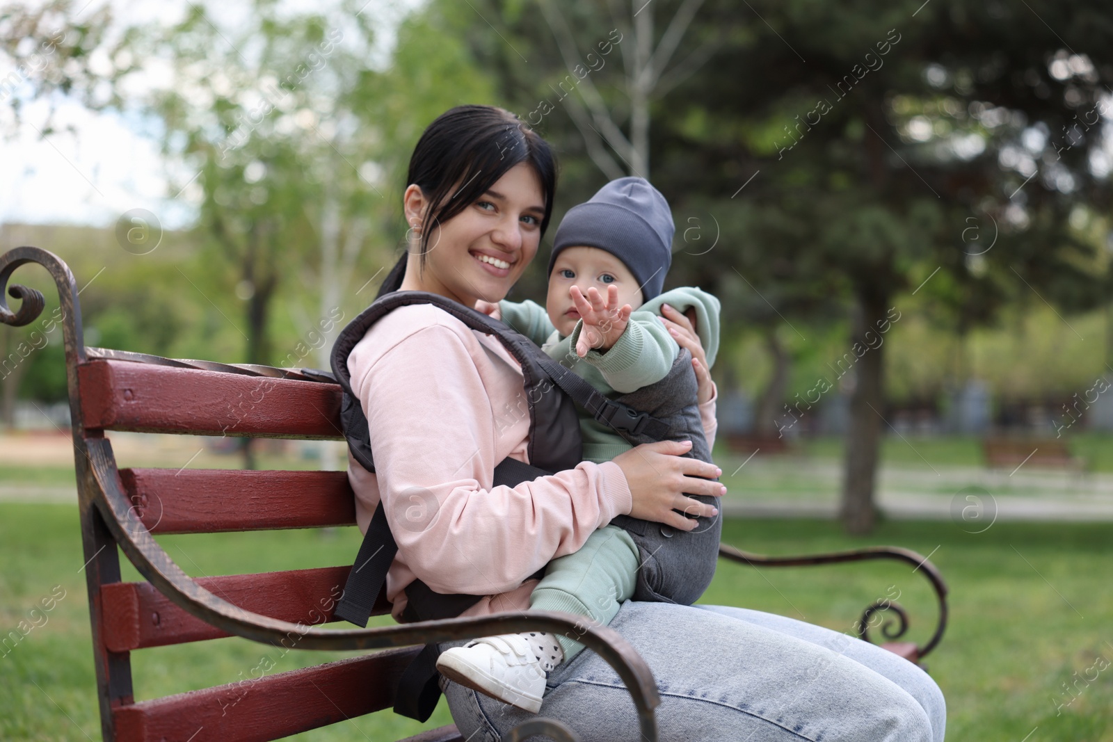 Photo of Mother holding her child in sling (baby carrier) on bench in park