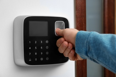 Man scanning fingerprint on alarm system indoors, closeup