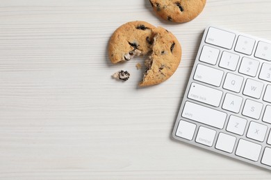 Photo of Chocolate chip cookies and keyboard on white wooden table, flat lay. Space for text